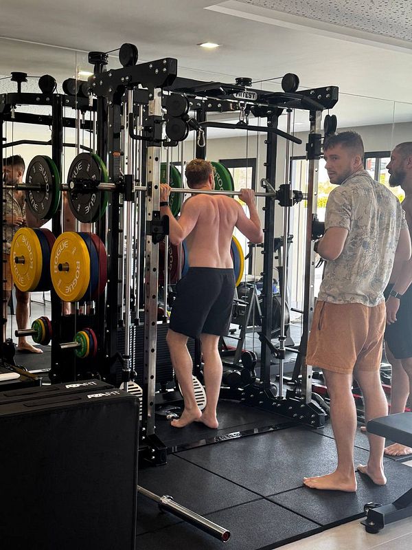 A group of men is engaged in a workout session at a gym, focusing on weightlifting.