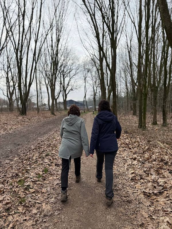 Two women are walking hand in hand along a forest path.