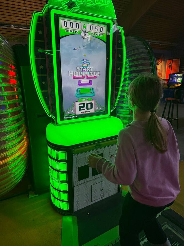 A child is playing a ticket redemption arcade game in a game hall.