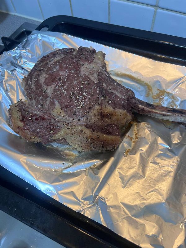 A close-up image of a cooked steak seasoned and garnished with herbs, displayed on a rustic surface.