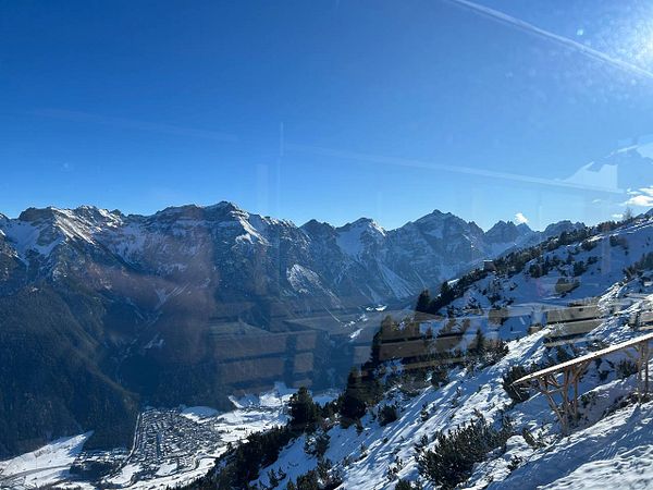 Snowboarder making a jump in a snowy mountainous landscape under a blue sky with clouds.