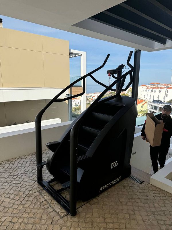 A large stair machine is positioned on a terrace with a person carrying a box nearby.