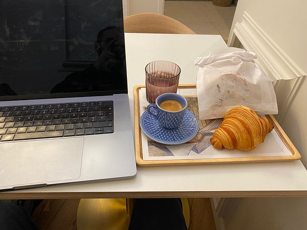 A cozy breakfast setup featuring a laptop, coffee, and pastries.