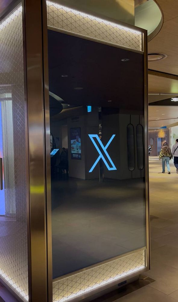 A sleek digital display featuring a prominent 'X' logo is situated in a modern indoor space.