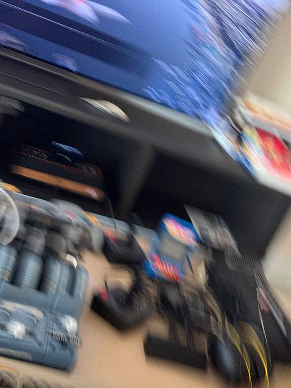 A cluttered workspace featuring various electronic devices and a blurred television screen.