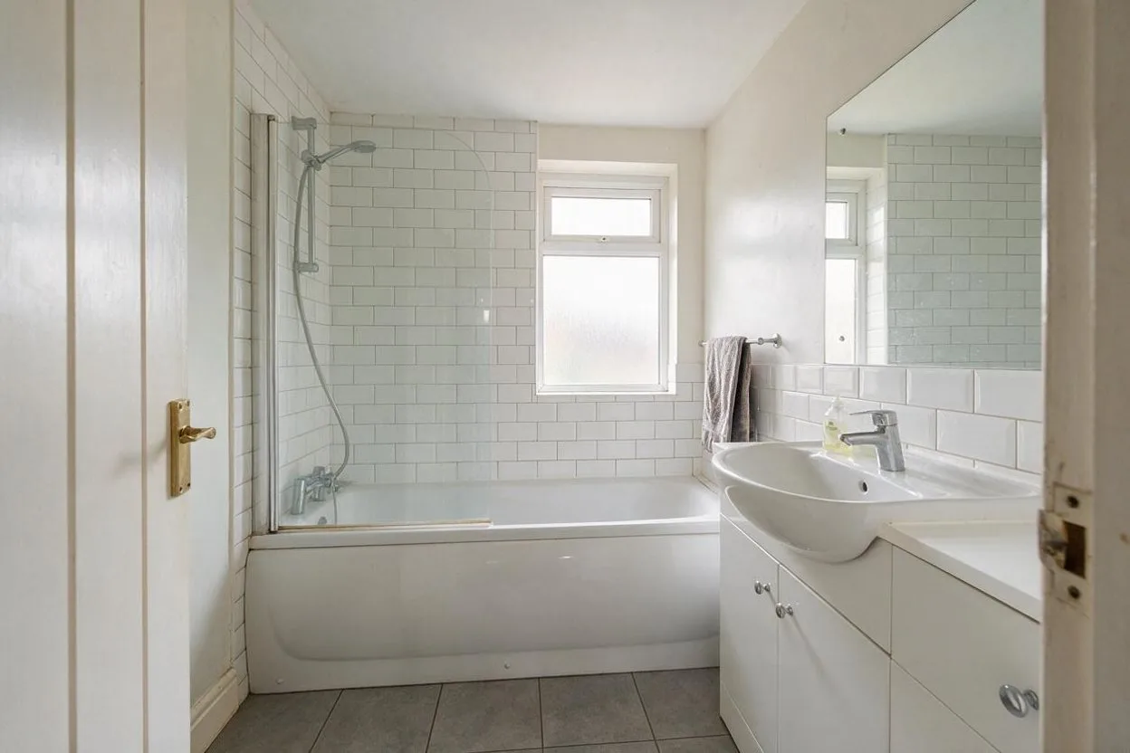 A plain white bathroom with metro tiles and a bath with a shower screen