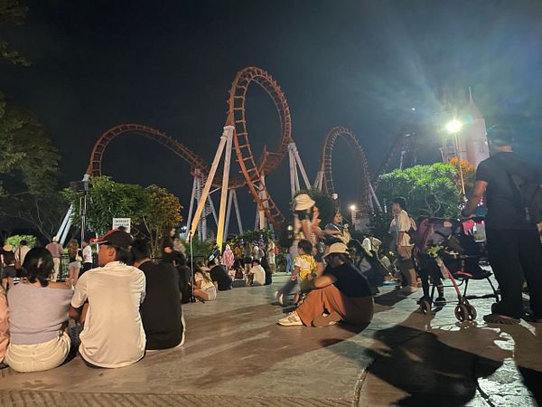 A lively scene at an amusement park featuring a roller coaster and groups of people enjoying the evening.