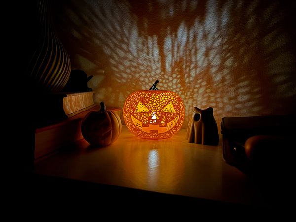 A beautifully lit Halloween pumpkin sits on a shelf surrounded by decorative items.