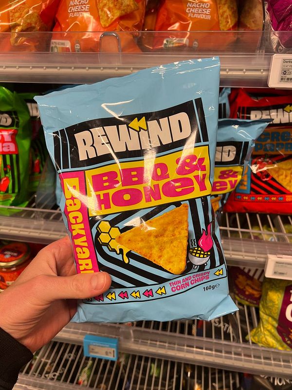 A person is holding a bag of BBQ & Honey flavored corn chips in a grocery store aisle.