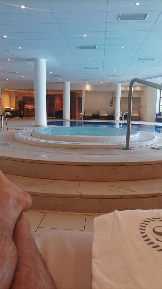 Black and white photo of a woman standing on a beach near the water, looking at the camera with hands behind her back.