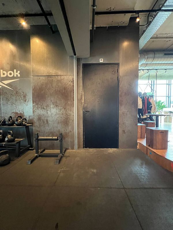 The image captures a gym interior featuring workout equipment and a black door.