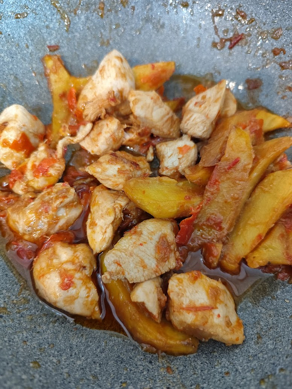 A close-up view of cooked chicken and potato pieces in a spicy sambal sauce.