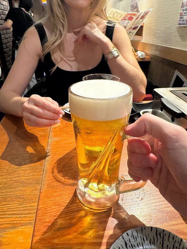 A hand holding a large glass of Sapporo beer is prominently featured in a lively dining setting.