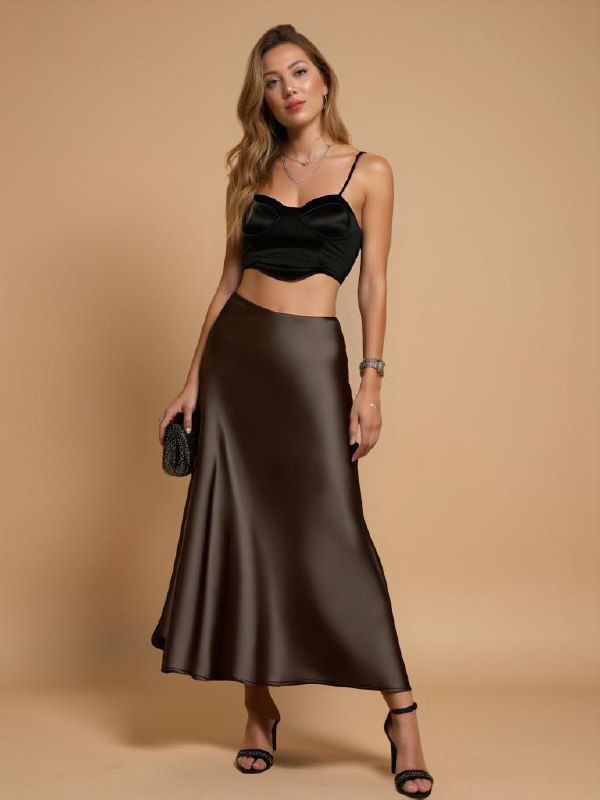 A model poses elegantly in a stylish outfit featuring a black crop top and a brown satin skirt.