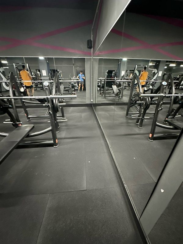 A gym interior featuring workout equipment and two individuals in the reflection of a mirror.