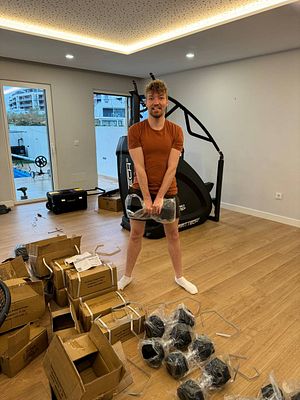 A person is assembling a home gym in a spacious room filled with unpacked equipment.