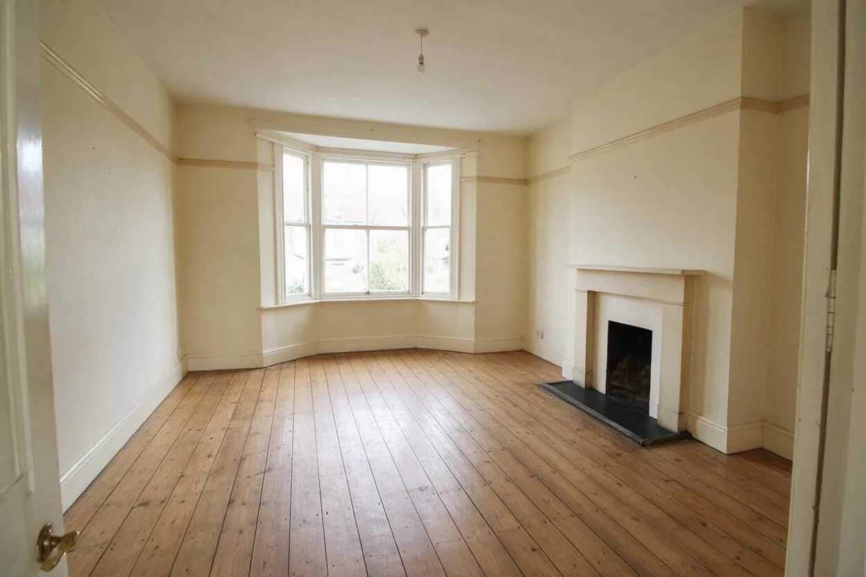 An empty living room with a bay window and a fireplace