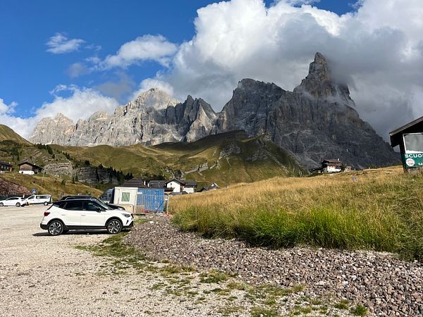 A scenic view of the Dolomites mountains with a parking area in the foreground.