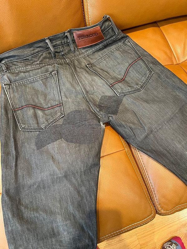 A pair of moto pants is laid out on a leather couch, showing signs of wear and a patching area.