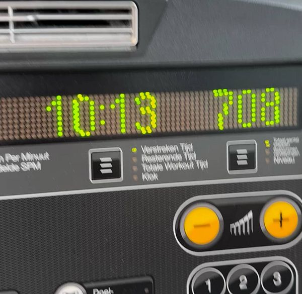 Man in gym attire performing a bent-over row exercise using a dumbbell on a workout bench next to a stairmaster machine.