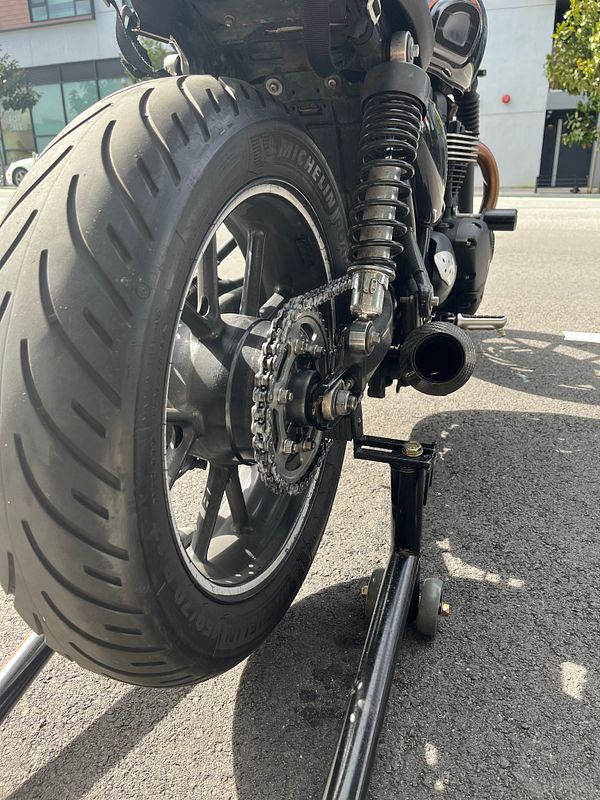 A motorcycle is positioned on a stand, showcasing its rear wheel and chain.