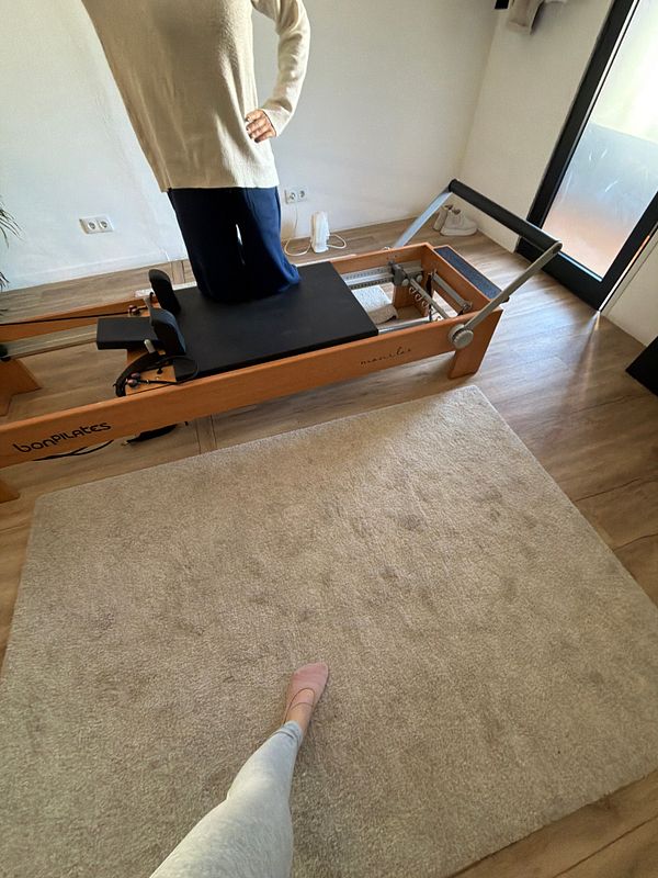 Woman in a Pilates studio performing an exercise on a reformer machine.