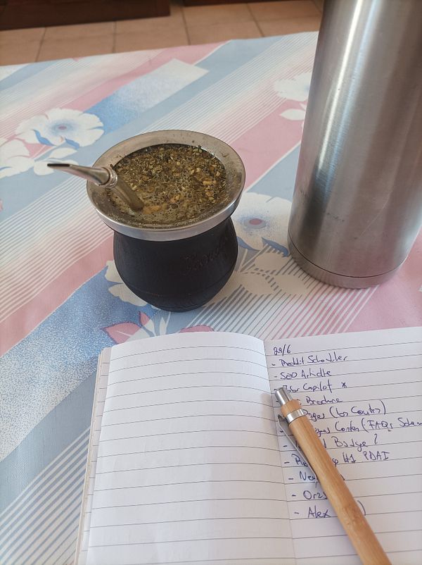 A workspace featuring a traditional mate drink, a notebook with tasks, and a thermos.