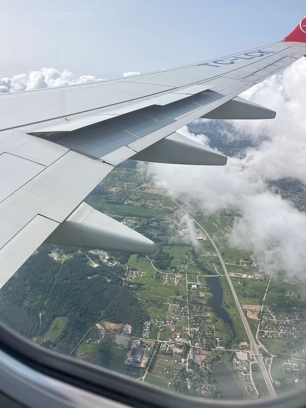 Aerial view from an airplane wing over a green landscape with scattered clouds.