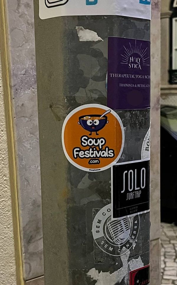 A sticker promoting 'Soup Festivals' is affixed to a pole covered in various other stickers.