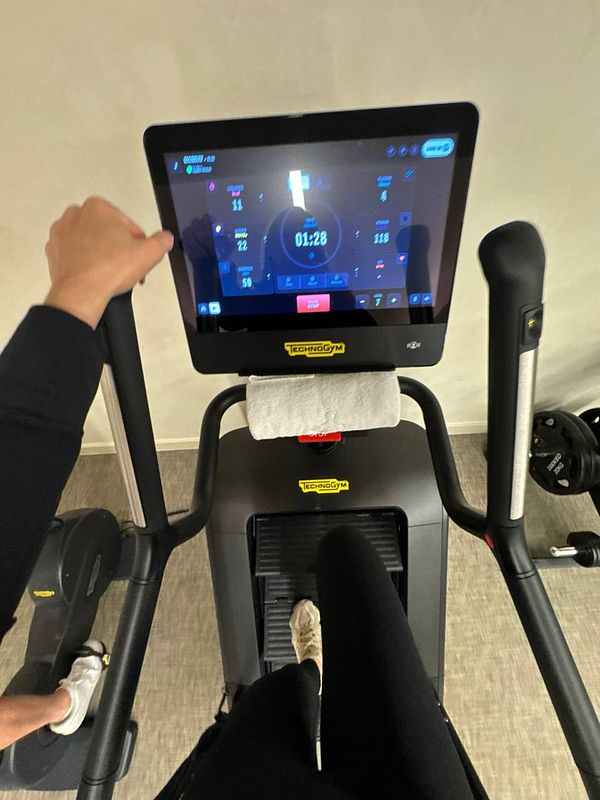 A person is exercising on a Technogym elliptical machine in a gym setting.