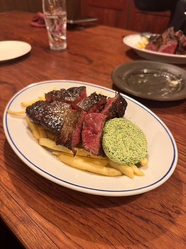A plate of steak served with fries and a green herb butter in a restaurant setting.