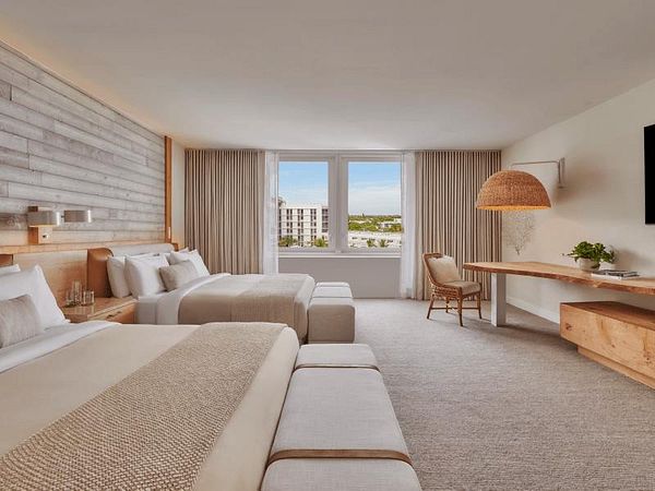 A modern hotel room featuring two beds, large windows, and stylish decor.