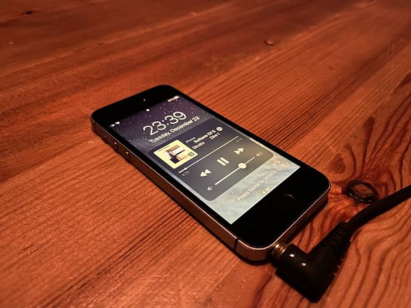 An iPhone SE 2016 is displayed on a wooden surface, showing the Spotify app interface.
