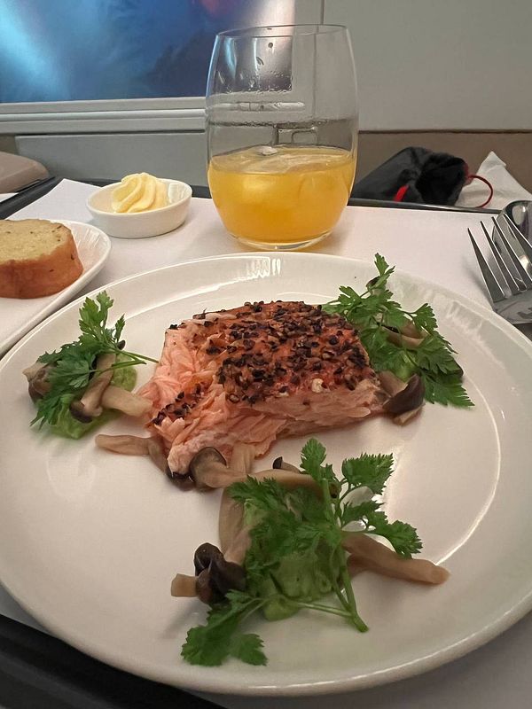 A gourmet meal served on an airplane tray featuring salmon, mushrooms, and a drink.