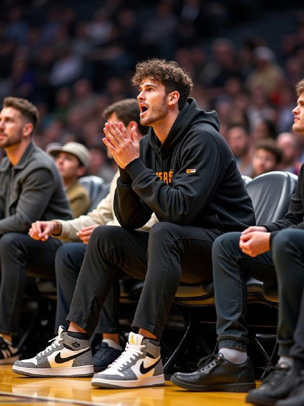 A young man is sitting on the sidelines of a basketball game, showing intense engagement.