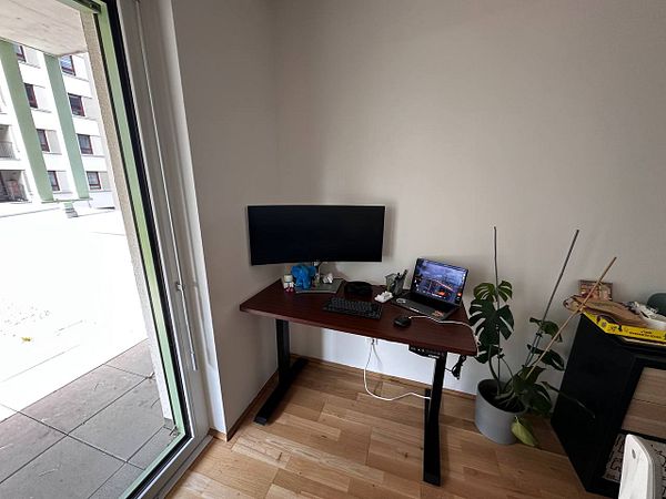 A modern desk setup in a bright corner of a room with a view outside.