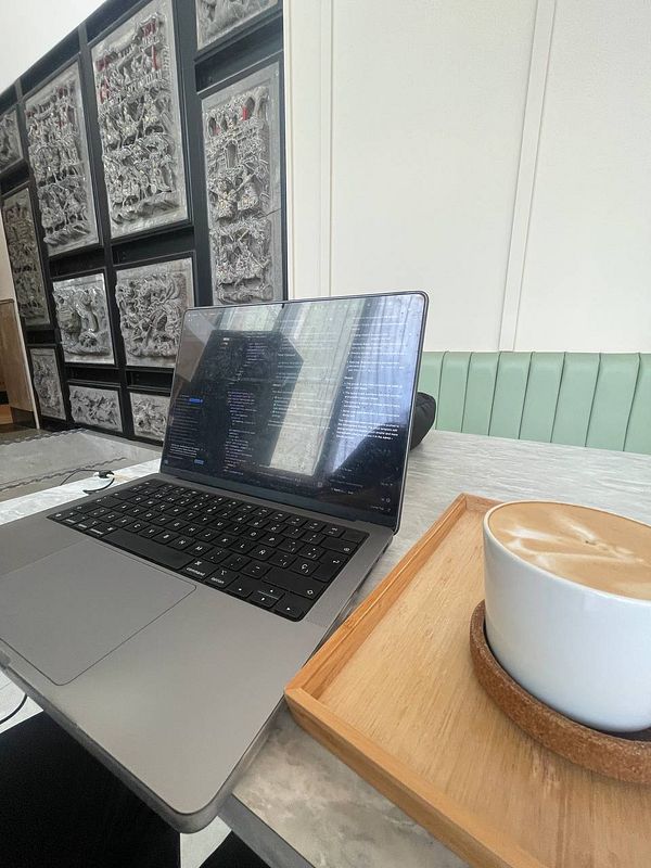 A laptop is set up on a table next to a cup of coffee in a stylish café environment.