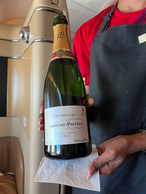 A flight attendant presents a bottle of Laurent-Perrier champagne onboard an aircraft.