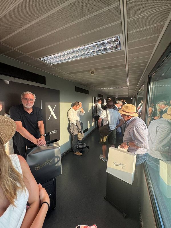 Passengers are waiting in a crowded jet bridge with no air conditioning, visibly uncomfortable in the heat.