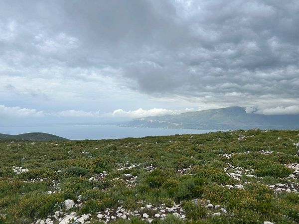 A panoramic view of a rugged landscape with rolling hills and a cloudy sky over a coastal area.