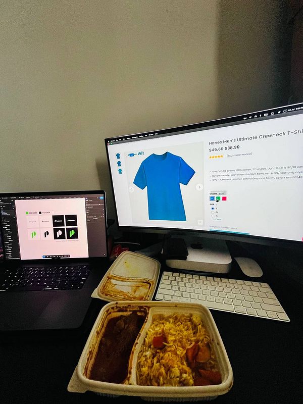 A workspace featuring two computer screens, a meal, and design software.