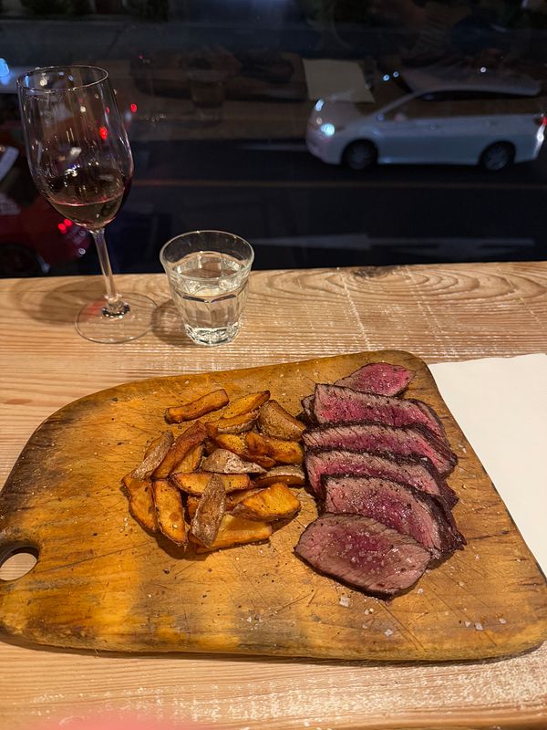 A beautifully presented plate of Kobe beef with fried potatoes and drinks.