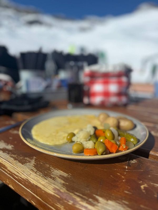 A plate of food is set on a wooden table with a snowy mountain backdrop.