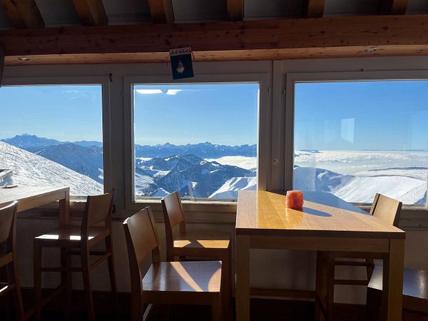 A cozy mountain restaurant with stunning views of snow-covered peaks and a bright blue sky.