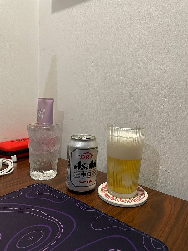 A cozy setup featuring a beer, a glass, and a skincare product on a wooden table.