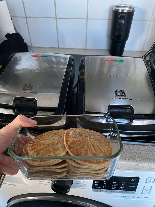 Stack of pancakes served with berries and pomegranate seeds on a white plate with a fork and knife.