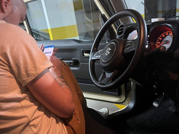 A black Suzuki Jimny 4x4 vehicle parked in front of a closed orange garage door.