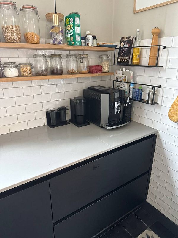 A kitchen coffee corner with a coffee machine and organized items on the countertop and shelves.