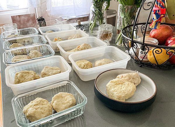 The image displays a kitchen countertop with several containers of freshly made cmoki and a fruit basket in the background.