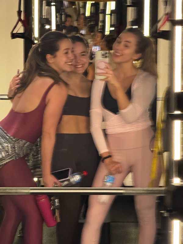 Three women pose together in a gym setting, capturing a fun moment in front of a mirror.